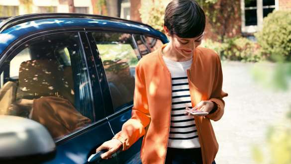 Ženska pogleda svoj pametni telefon in odpre vrata svojega BMW BMW Teleservices, ženska pogleda svoj pametni telefon in odpre vrata svojega BMW