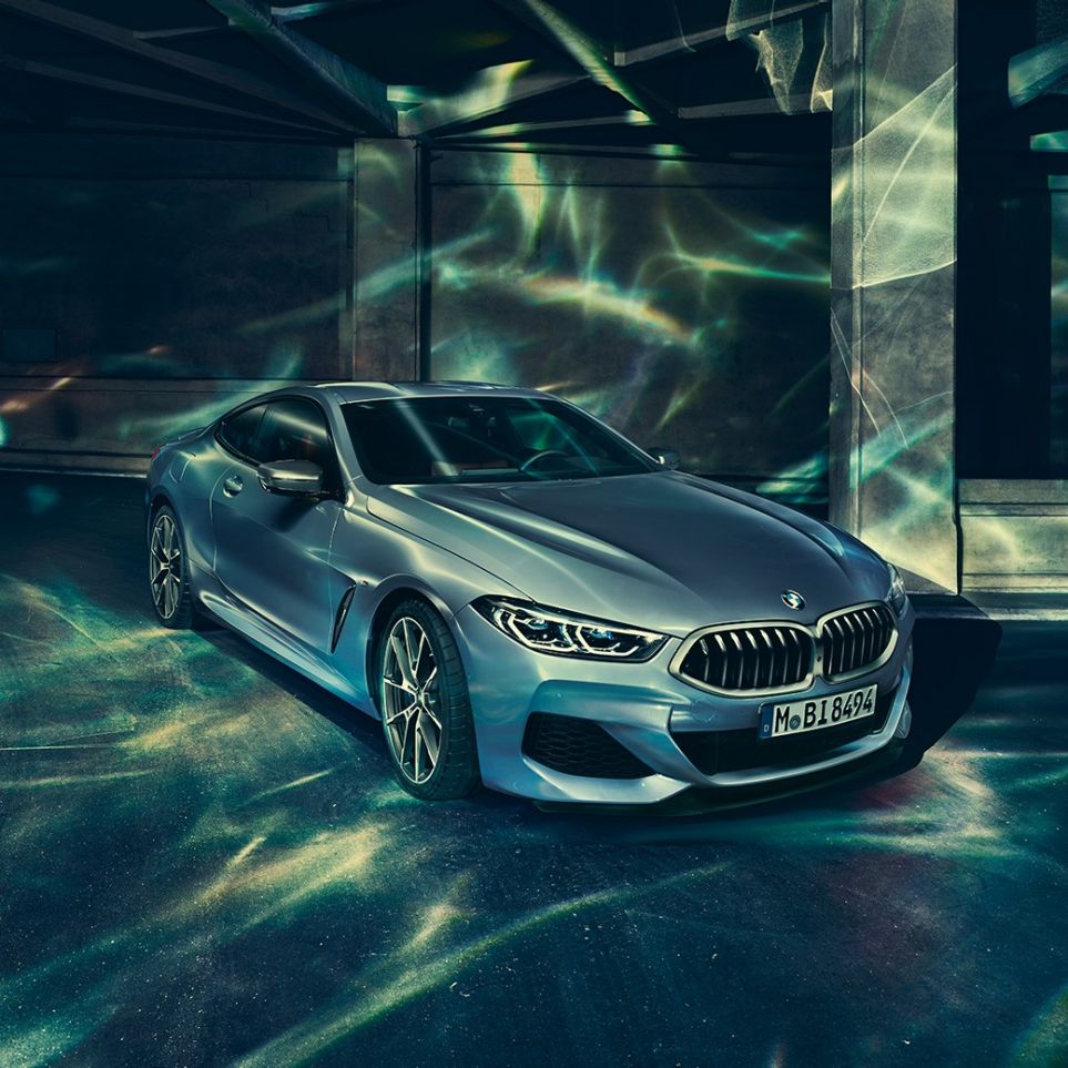 BMW M850i xDrive Coupé, v sprednjem polprofilu z leve strani. BMW M850i xDrive Coupé v kovinski barvi Barcelona Blue, v sprednjem polprofilu z leve strani, parkiran pred stavbo.