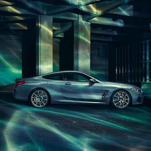 BMW M850i xDrive Coupé, v profilu. BMW M850i xDrive Coupé v kovinski barvi Barcelona Blue, v profilu, parkiran pred stavbo.