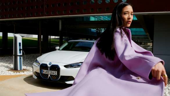 BMW Service Inclusive za električna vozila BMW Service Inclusive, ženska stoji pred BMW i4 pri polnilni postaji