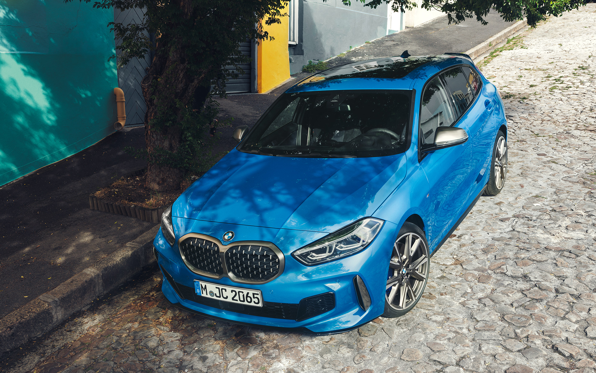 BMW serije 1, M135i, F40, ob cesti BMW serije 1, M135i, F40, kovinska barva Misano Blue, tričetrtinski pogled od spredaj med parkiranjem ob cesti iz ptičje perspektive
