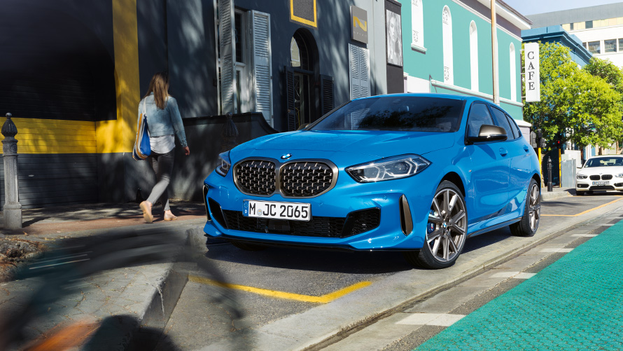 BMW serije 1, F40, kovinska barva Misano Blue, tričetrtinski pogled od spredaj BMW serije 1, F40, kovinska barva Misano Blue, tričetrtinski pogled od spredaj med parkiranjem ob robu ceste z žensko