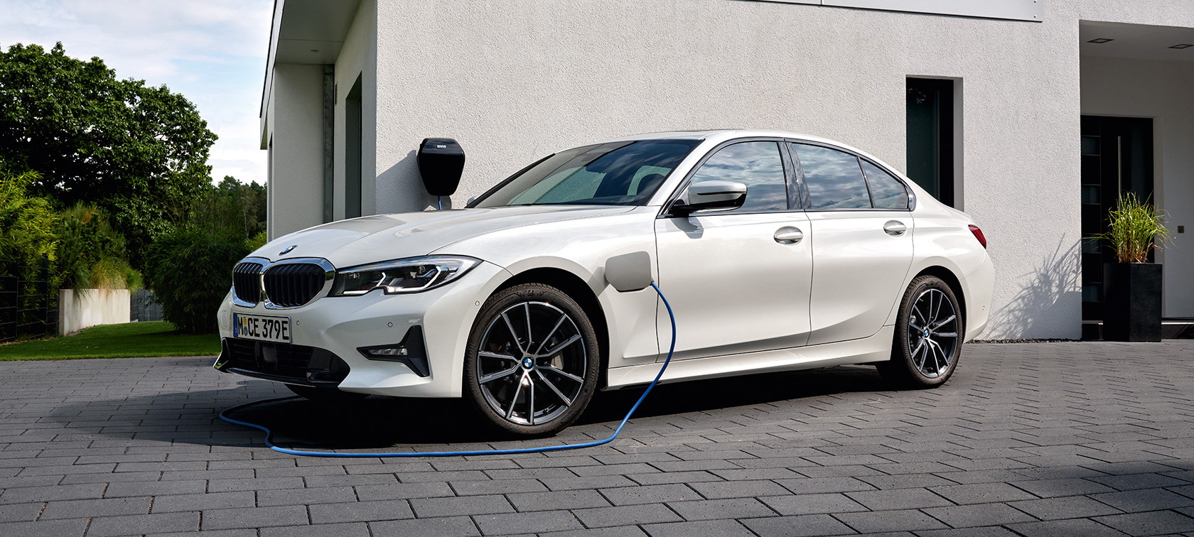 Priključni hibrid BMW serije 3 Limuzina, 2021, G20, tričetrtinski stranski pogled, polnjenje Priključni hibrid BMW serije 3 Limuzina, 2021, G20, tričetrtinski stranski pogled, polnjenje pred garažo