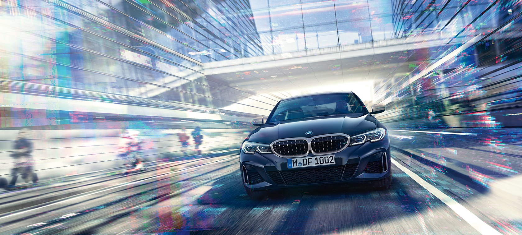 BMW serije 3 Limuzina, pogled od spredaj BMW M340i xDrive. Pogled od spredaj vozečega BMW M340i xDrive Limuzina med mestnimi steklenimi stavbami.