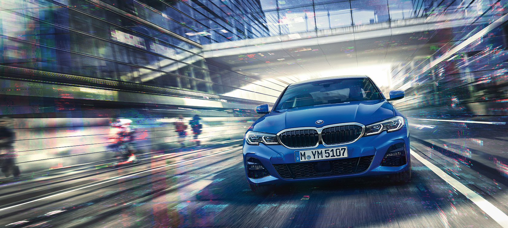 Pogled od spredaj na BMW serije 3 Limuzina (G20) med vožnjo podnevi pod stekleno stavbo.