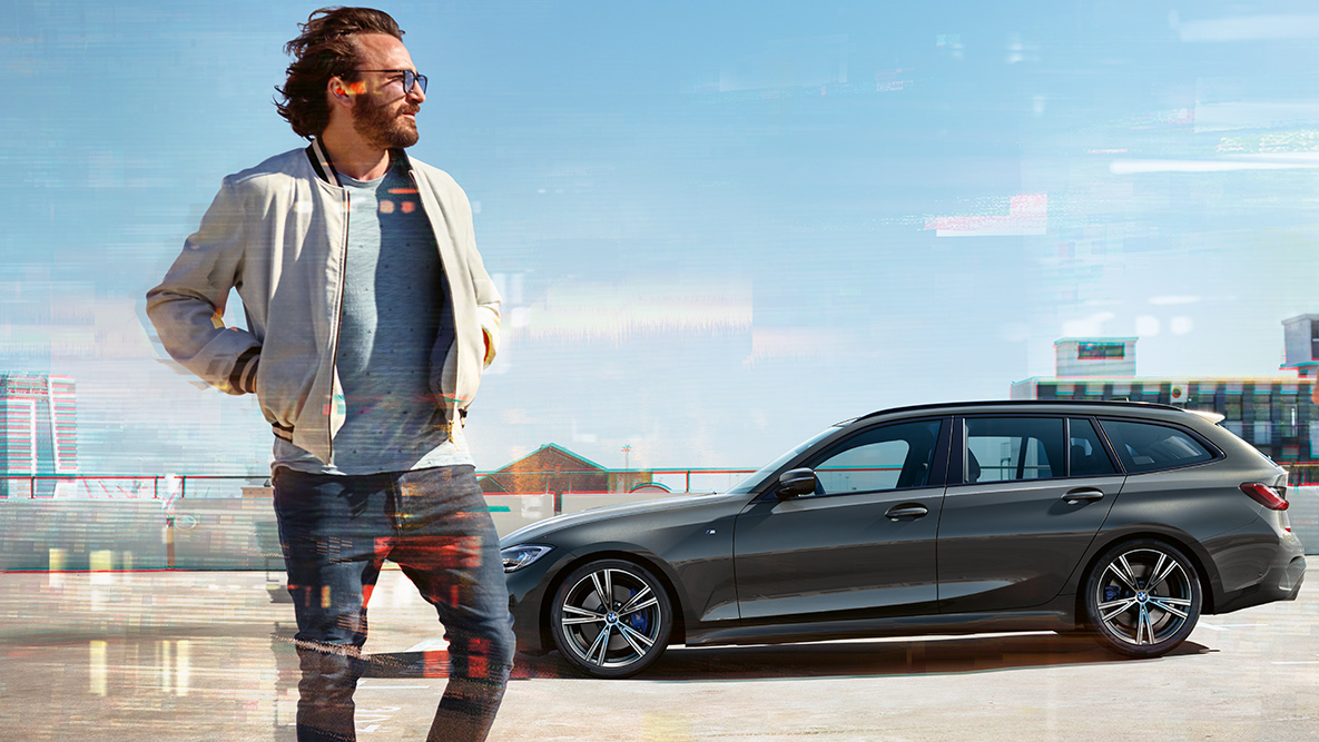 BMW serije 3 Touring (G21), tričetrtinski posnetek od spredaj, oblika BMW serije 3 Touring (G21), barva Dravit Grey, tričetrtinski posnetek od spredaj med vožnjo na mostu v podeželskem okolju