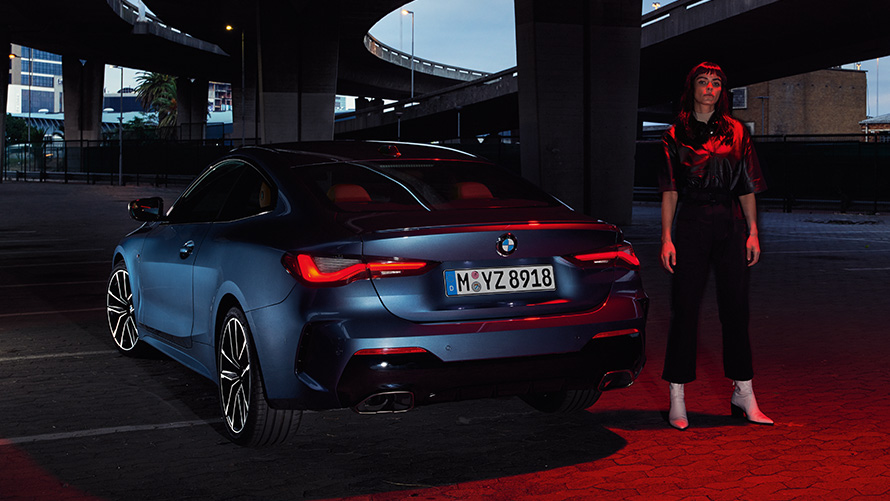 BMW serije 4 Coupé (G22), kovinska barva Artic Race Blue, pogled od zadaj z osebo BMW serije 4 Coupé (G22), kovinska barva Artic Race Blue, pogled od zadaj z osebo