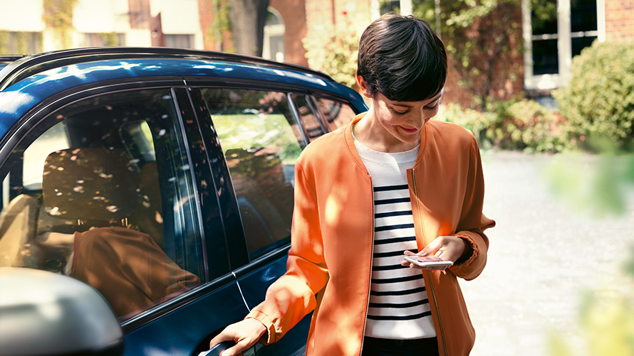 BMW Service, ženska s pametnim telefonom stoji pred vrati svojega BMW BMW Service, ženska s pametnim telefonom stoji pred vrati svojega BMW