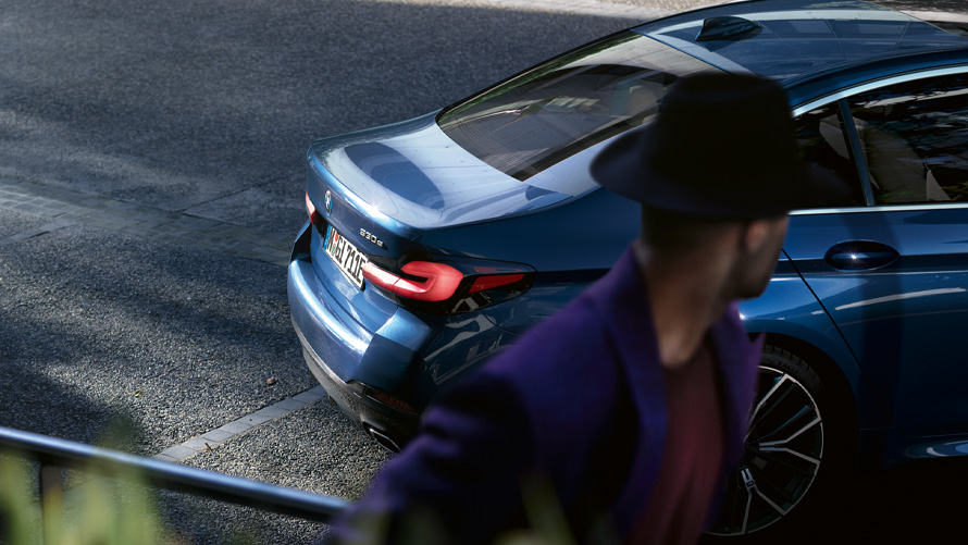 BMW serije 5 Limuzina (G30), kovinska barva Phytonic Blue BMW serije 5 Limuzina (G30), kovinska barva Phytonic Blue, pogled od spredaj na parkirišče z osebo v ospredju