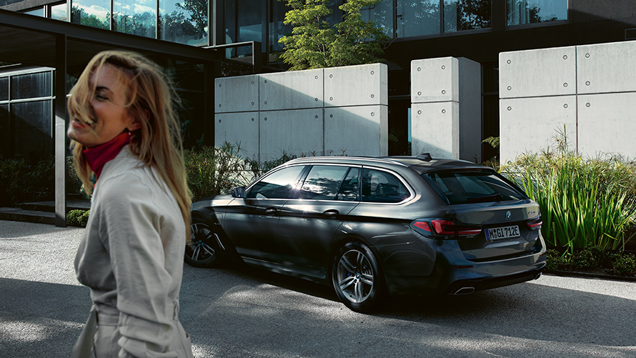 BMW serije 5 Touring, G31, LCI, ženska, kovinska barva Sophisto Grey Brilliant Effect, sedemosminski stranski pogled BMW serije 5 Touring, G31, osvežitev 2020, ženska pred parkiranim vozilom, kovinska barva Sophisto Grey Brilliant Effect, sedemosminski stranski pogled