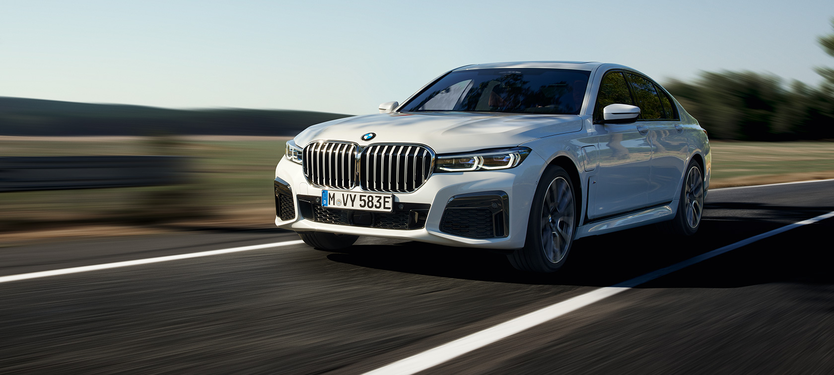 Priključni hibrid BMW 745e Limuzina, G11, G12, kovinska barva Mineral White, tričetrtinski pogled od spredaj Priključni hibrid BMW 745e Limuzina, G11, G12, kovinska barva Mineral White, tričetrtinski pogled od spredaj med vožnjo po podeželski cesti