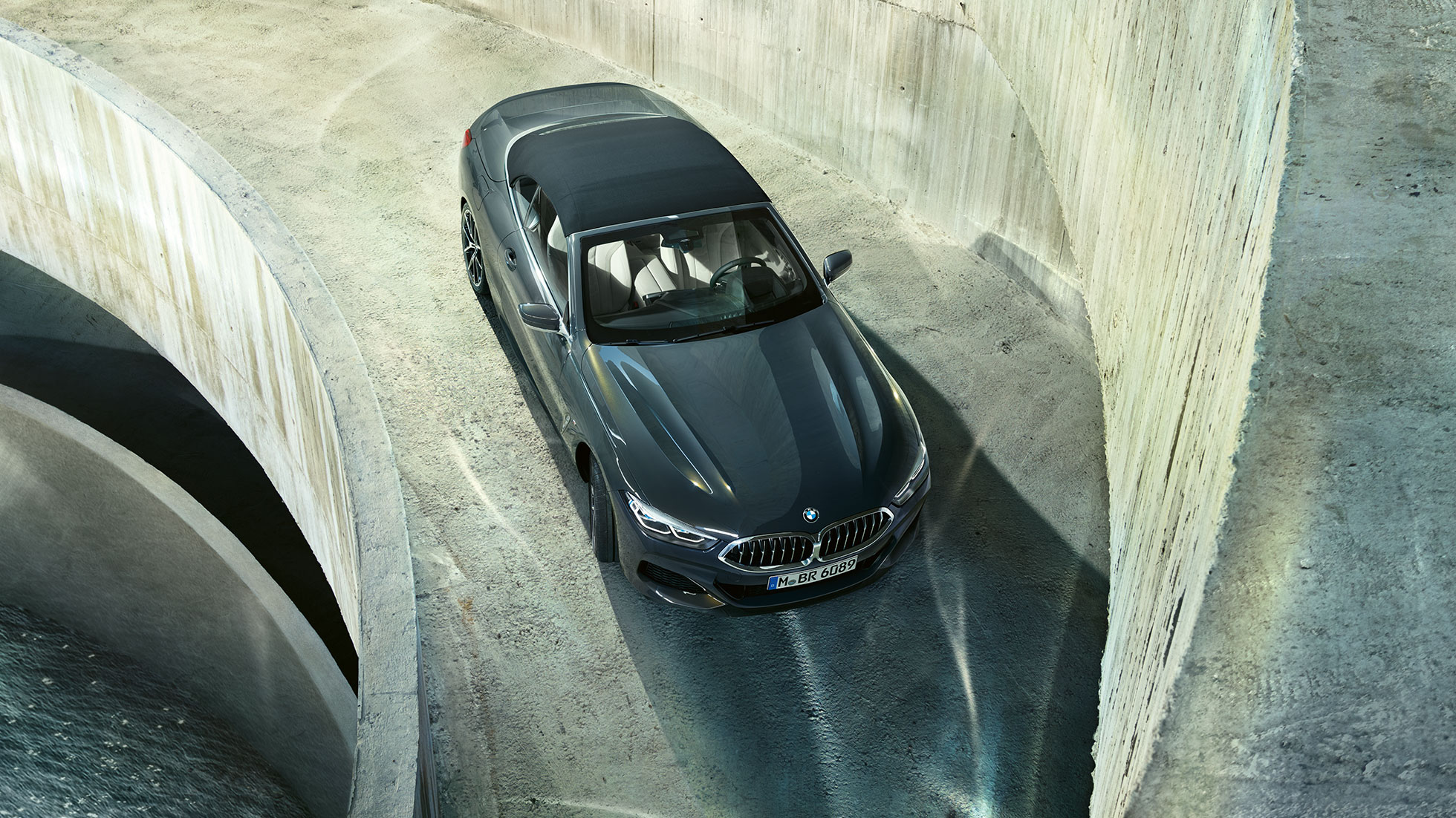 BMW M850i xDrive v kovinskem odtenku Dravit Grey z mehko črno streho iz ptičje perspektive. BMW M850i xDrive v kovinskem odtenku Dravit Grey z mehko črno streho iz ptičje perspektive.