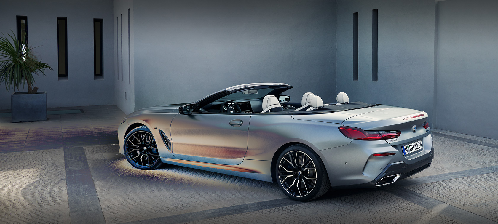 Novi BMW serije 8 Cabrio, G14, LCI, osvežitev 2022, lakiranje BMW Individual v kovinski barvi Frozen Pure Grey, stranski pogled med mirovanjem pred stavbo z manekenom