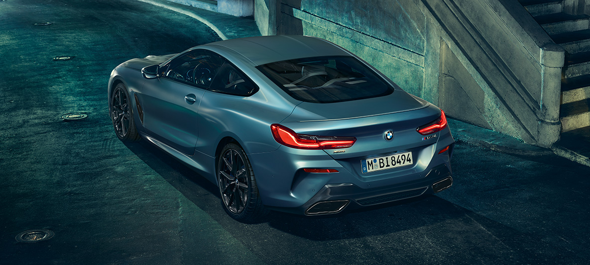 BMW M850i Coupé First Edition, polprofil od zadaj Fotografija vozila BMW M850i Coupé First Edition v polprofilu od zadaj v urbanem okolju.