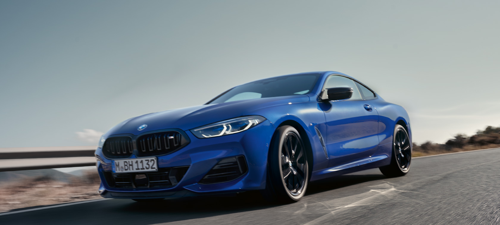 BMW serije 8 Coupé G15 LCI Facelift 2022 BMW M850i xDrive M Portimao modra kovinska slika spredaj pod nizkim kotom BMW serije 8 Coupé G15 LCI Facelift 2022 BMW M850i xDrive M Portimao modra kovinska spredni posnetek pod nizkim kotom vožnje po podeželski cesti s hribi v ozadju