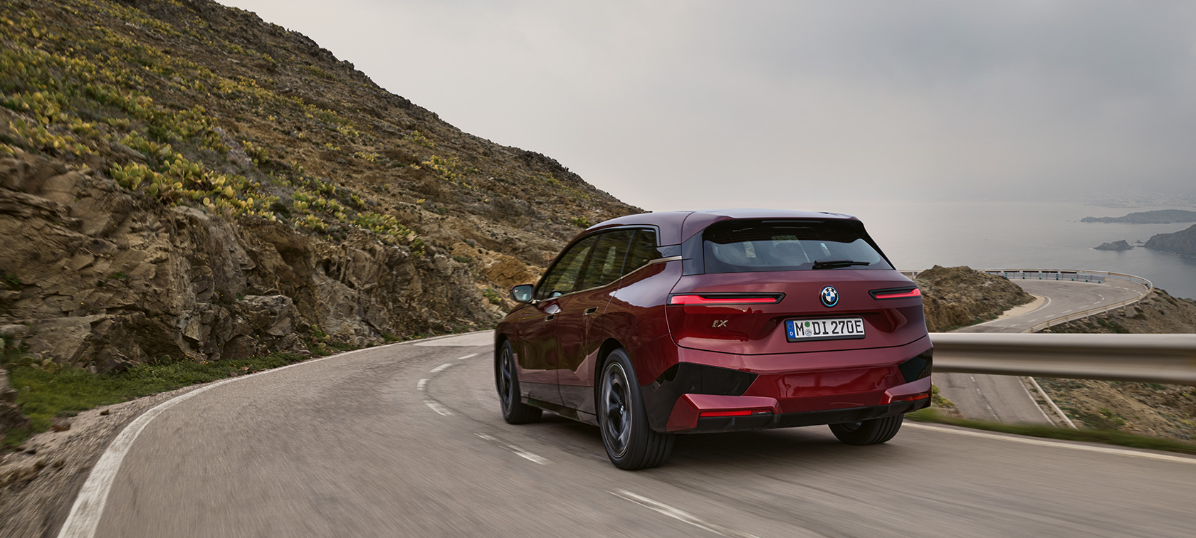 BMW iX, i20, 2021, električni SUV, BMW iX xDrive50, vožnja po obalni cesti BMW iX, i20, 2021, električni SUV, BMW iX xDrive50, barva Aventurin Red, pogled od zadaj med vožnjo po obalni cesti