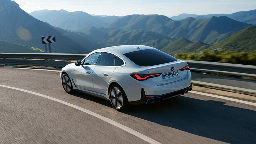 BMW i4 eDrive40, G26, 2021, tričetrtinski pogled od zadaj med vožnjo BMW i4 eDrive40, G26, 2021, barva Mineral White, tričetrtinski pogled od zadaj med vožnjo