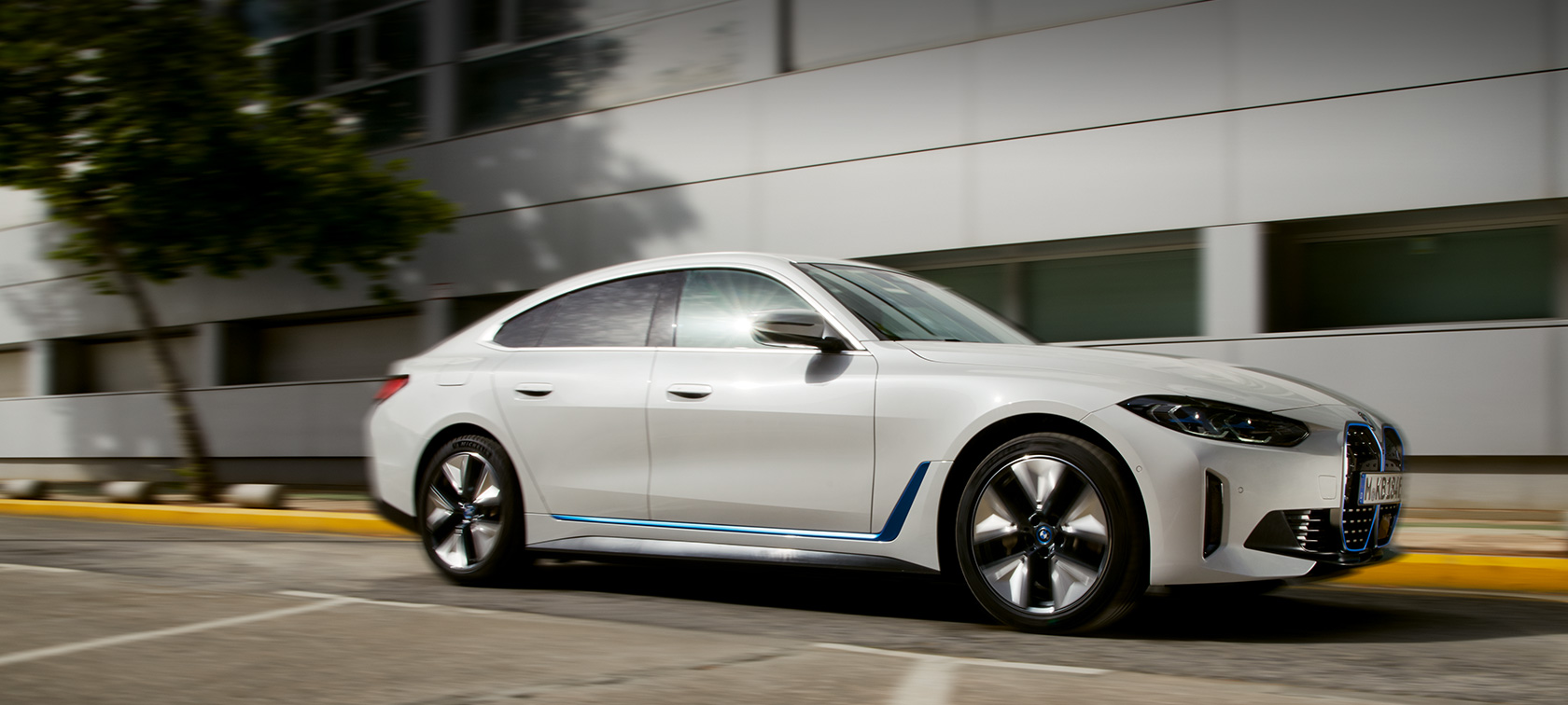 BMW i4 eDrive40, G26, 2021, tričetrtinski stranski pogled med vožnjo pred stavbo BMW i4 eDrive40, G26, 2021, tričetrtinski stranski pogled med vožnjo pred stavbo