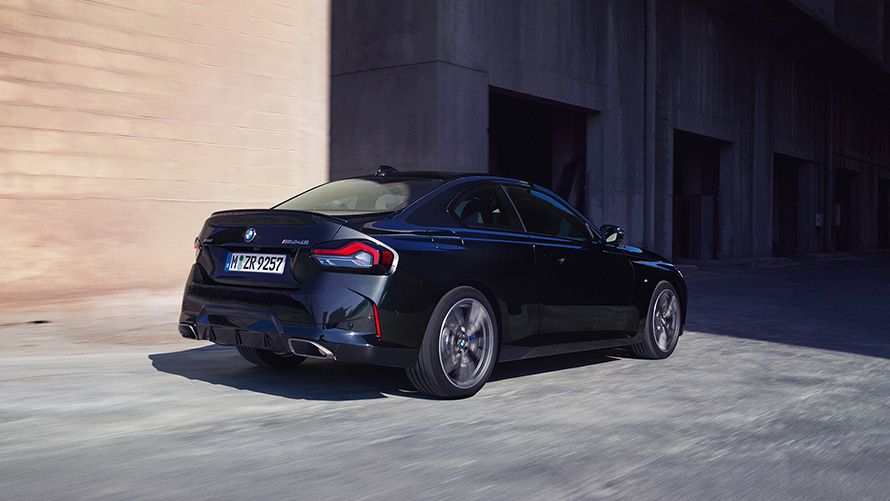 BMW M240i xDrive Coupé, G42, 2021, tričetrtinski pogled od zadaj med mirovanjem BMW M240i xDrive Coupé, G42, 2021, kovinska barva Black Sapphire, tričetrtinski pogled od zadaj med mirovanjem pred skladiščem