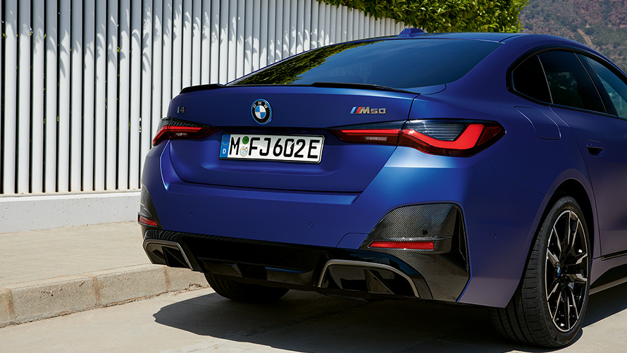 BMW i4 M50, G26, 2021, lakiranje BMW Individual v kovinski barvi Frozen Portimao Blue, tričetrtinski pogled od zadaj med mirovanjem ob beli ograji