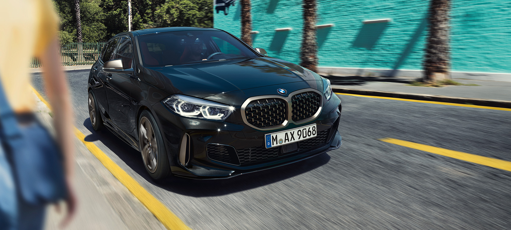 BMW M135i xDrive, tričetrtinski pogled od spredaj. BMW M135i xDrive v kovinski barvi Black Sapphire, tričetrtinski pogled od spredaj med vožnjo.