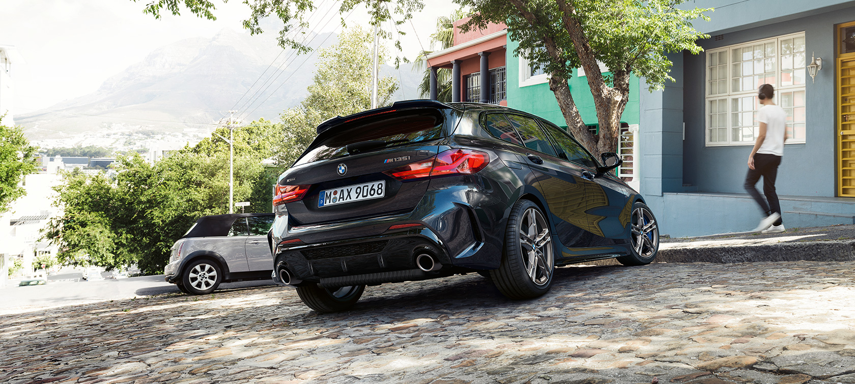 BMW M135i xDrive, tričetrtinski pogled od zadaj. BMW M135i xDrive v kovinski barvi Black Sapphire, tričetrtinski pogled od zadaj na parkirišče pred stanovanjsko stavbo.