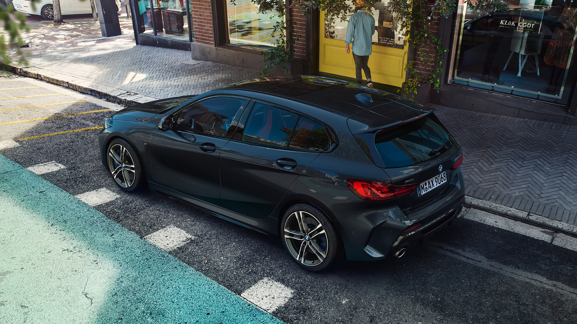 BMW M135i xDrive, parkiranje. BMW M135i xDrive v kovinski barvi Black Sapphire, stranski pogled iz ptičje perspektive na parkirišče.