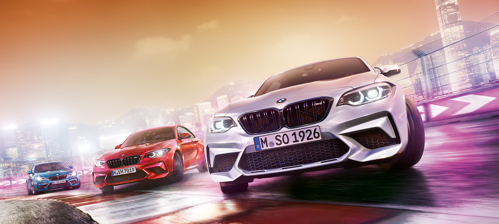 BMW M2 Competition v akciji Trije BMW M2 Competition drsijo bočno na stezi pred nočno kuliso velemesta.