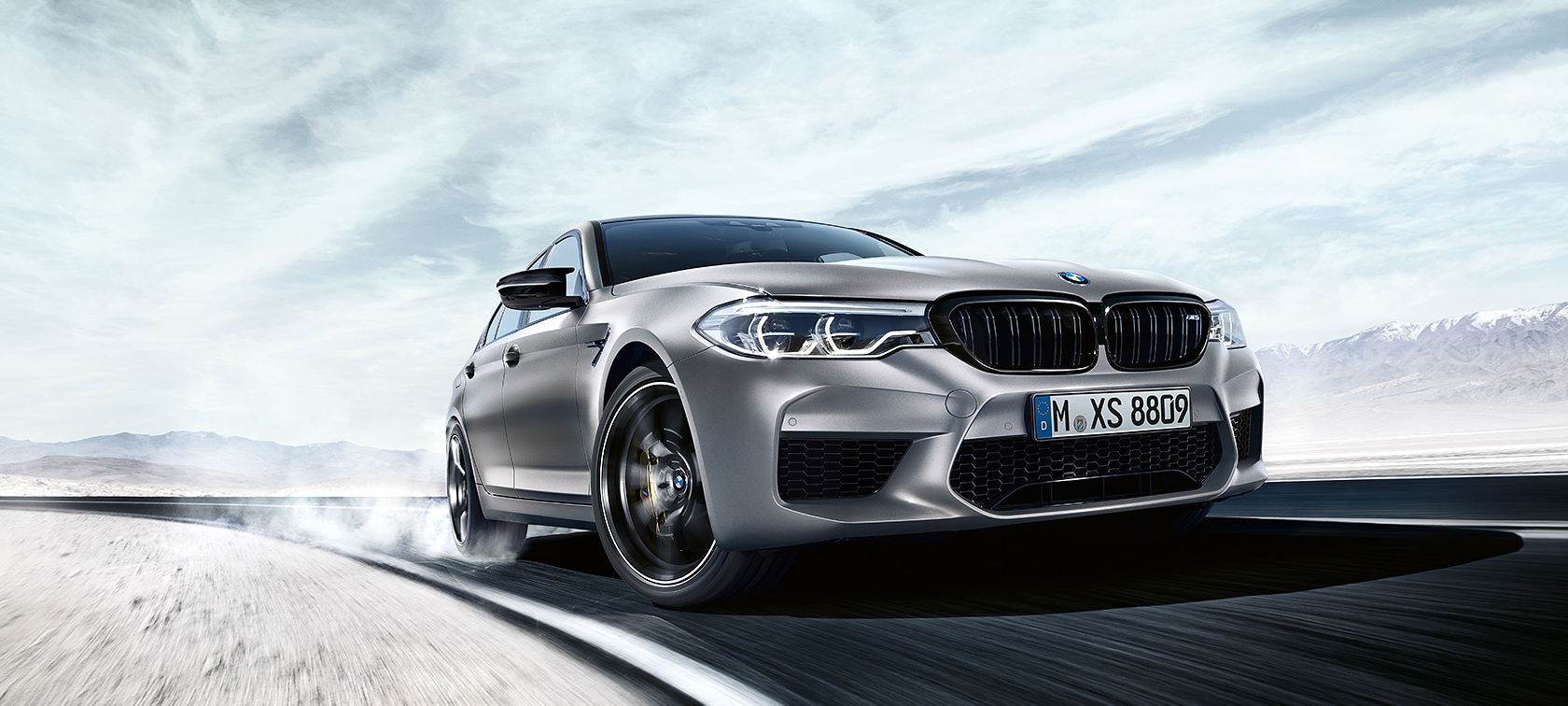 BMW M5 Competition v akciji Siv BMW M5 Competition vozi na avtocesti pred puščavsko pokrajino