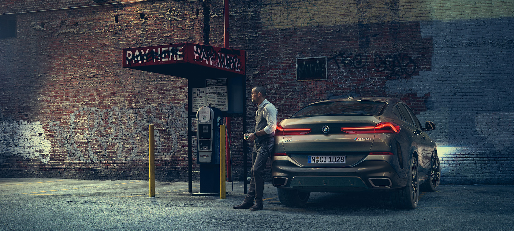 Zadek BMW X6 M50i. Moški se naslanja na zadek BMW X6 M50i.