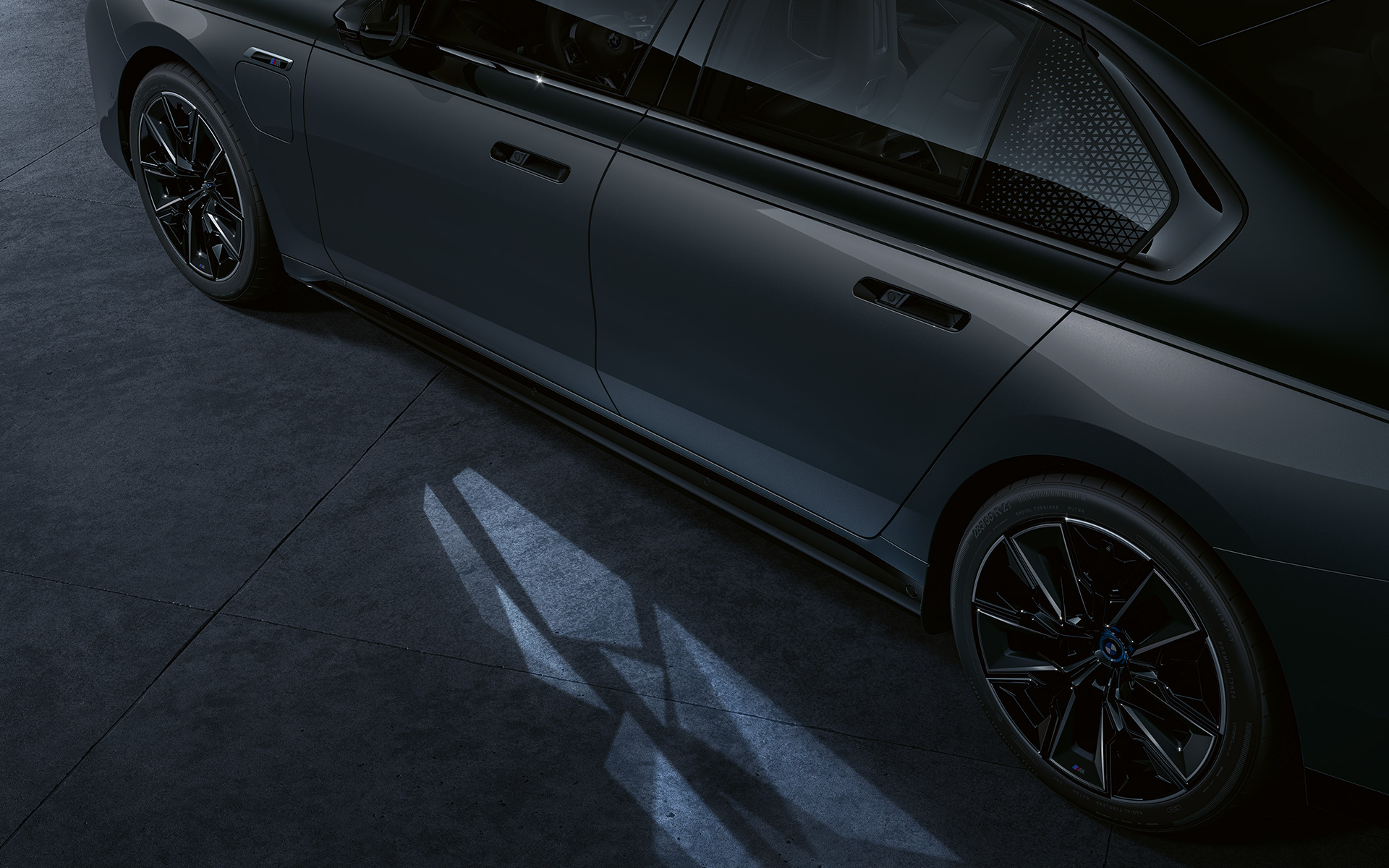 BMW M760e xDrive Limuzina, G70, koncept razsvetljave, dvobarvno lakiranje BMW Individual v kovinski barvi Black Sapphire, lakiranje BMW Individual v kovinski barvi Dravite Grey, stranski pogled od blizu z vklopljeno funkcijo Welcome Light Carpet