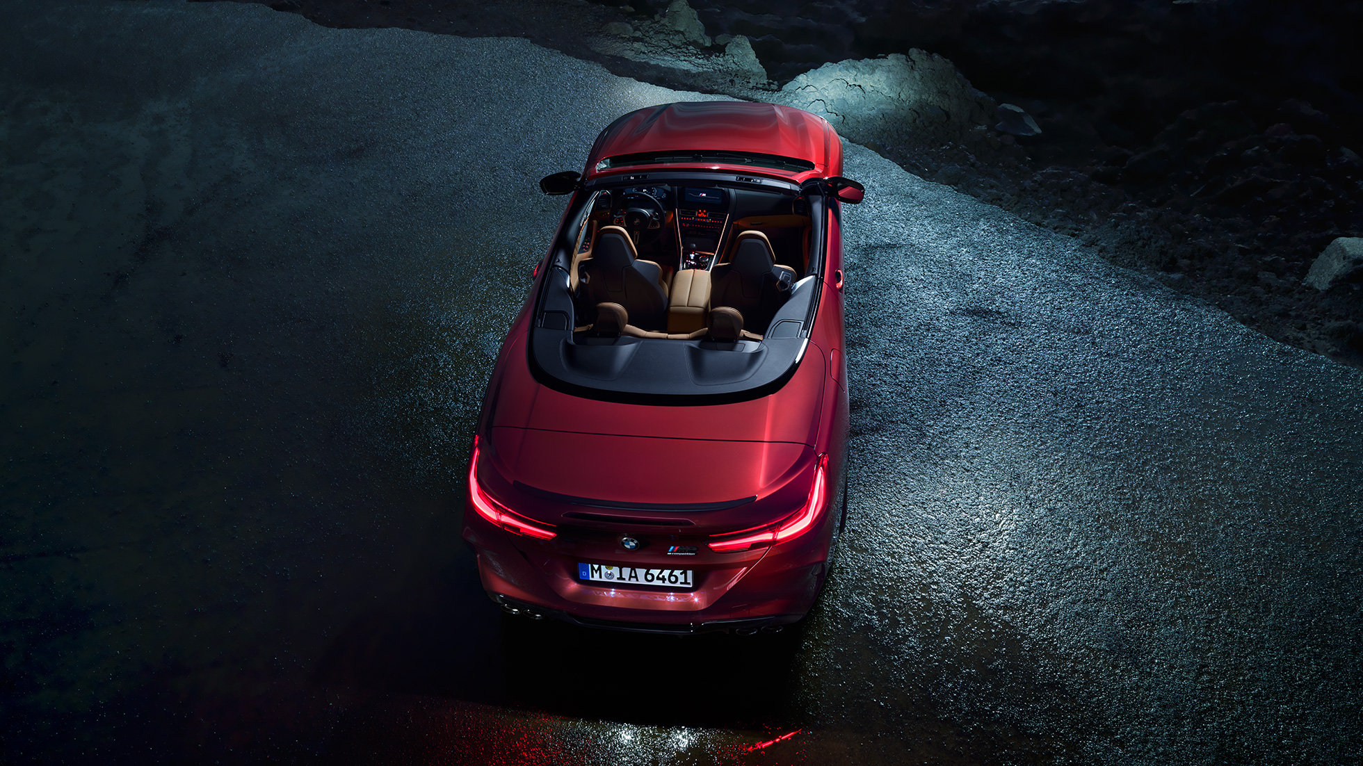 BMW M8 Competition Cabrio, iz ptičje perspektive. BMW M8 Competition Cabrio v kovinski barvi Motegi Red z odprto platneno streho, iz ptičje perspektive, ponoči parkiran na asfaltu.
