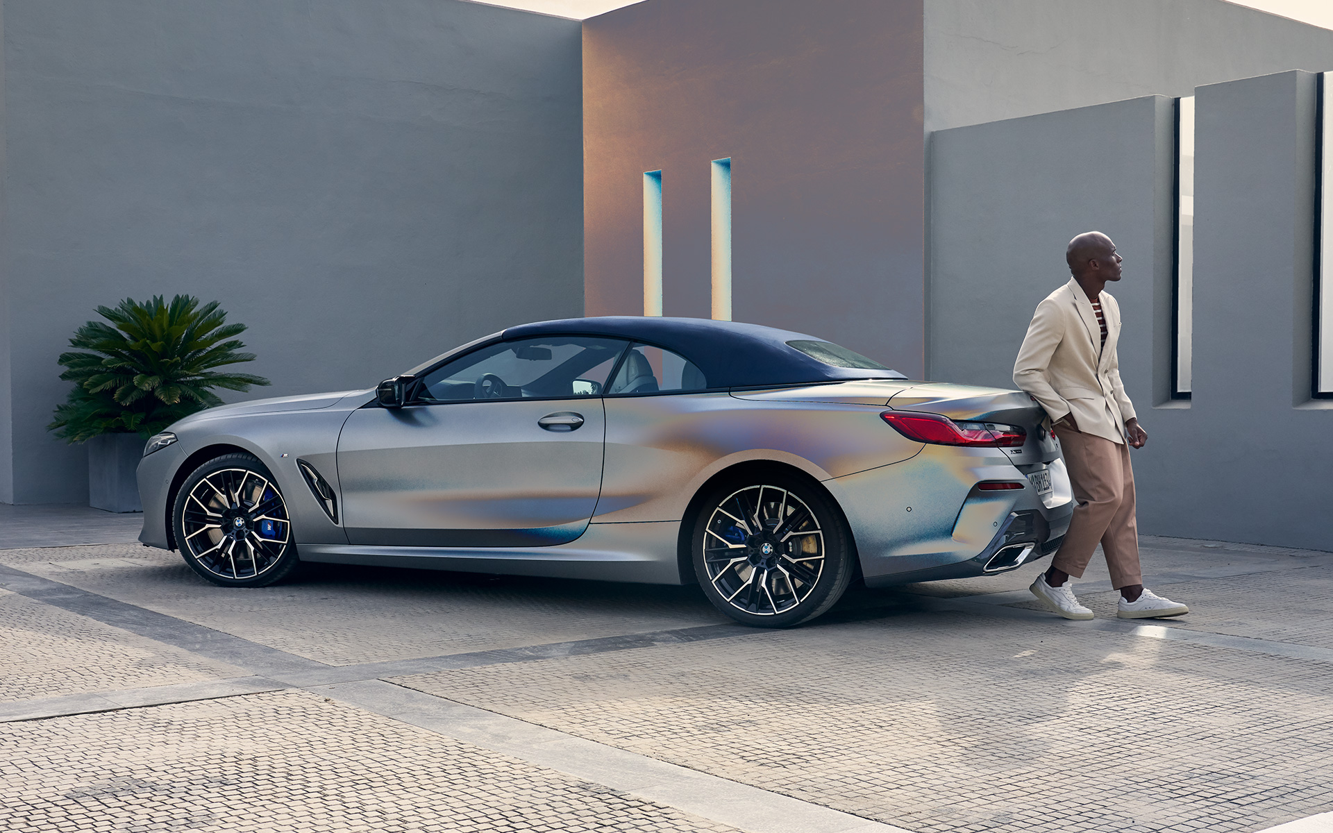 BMW M850i xDrive Cabrio, G14, LCI, osvežitev 2022, tričetrtinski pogled od zadaj BMW M850i xDrive Cabrio, G14, LCI, osvežitev 2022, lakiranje BMW Individual v kovinski barvi Frozen Pure Grey, tričetrtinski pogled od zadaj z manekenko, naslonjeno na vozilo