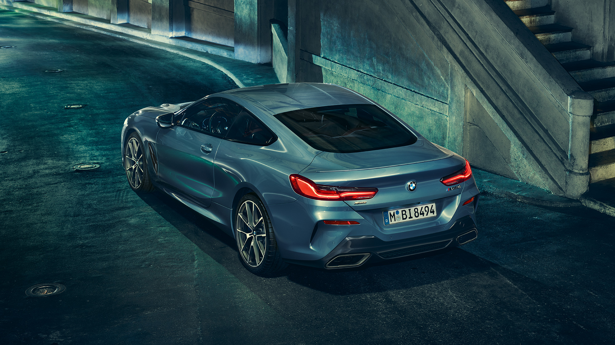 BMW M850i xDrive Coupé, v zadnjem polprofilu z leve strani. BMW M850i xDrive Coupé v kovinski barvi Barcelona Blue, v zadnjem polprofilu, parkiran ponoči.
