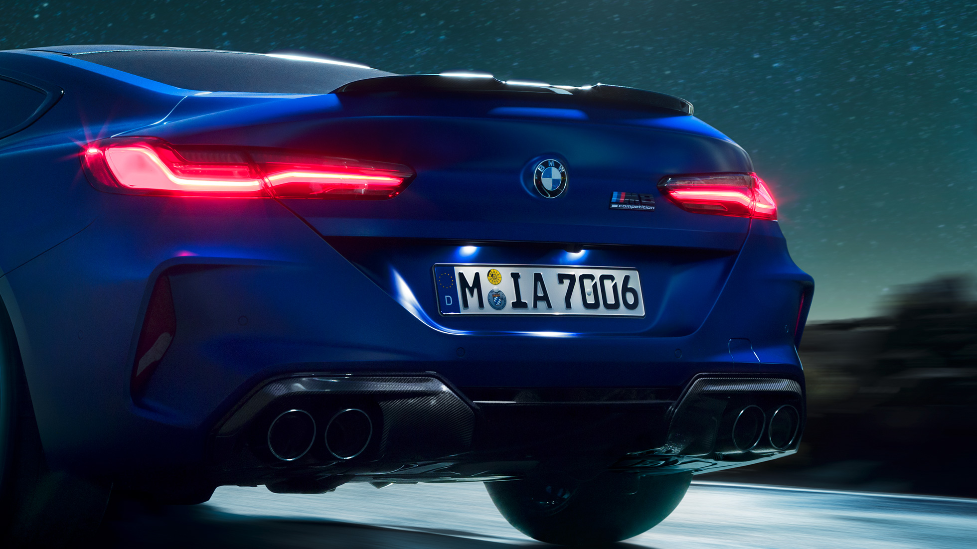 M difuzor v barvi Carbon Black. BMW M8 Competition Coupé v kovinski barvi Marina Bay Blue, povečan posnetek zadnjega dela ponoči z M difuzorjem v barvi Carbon Black.