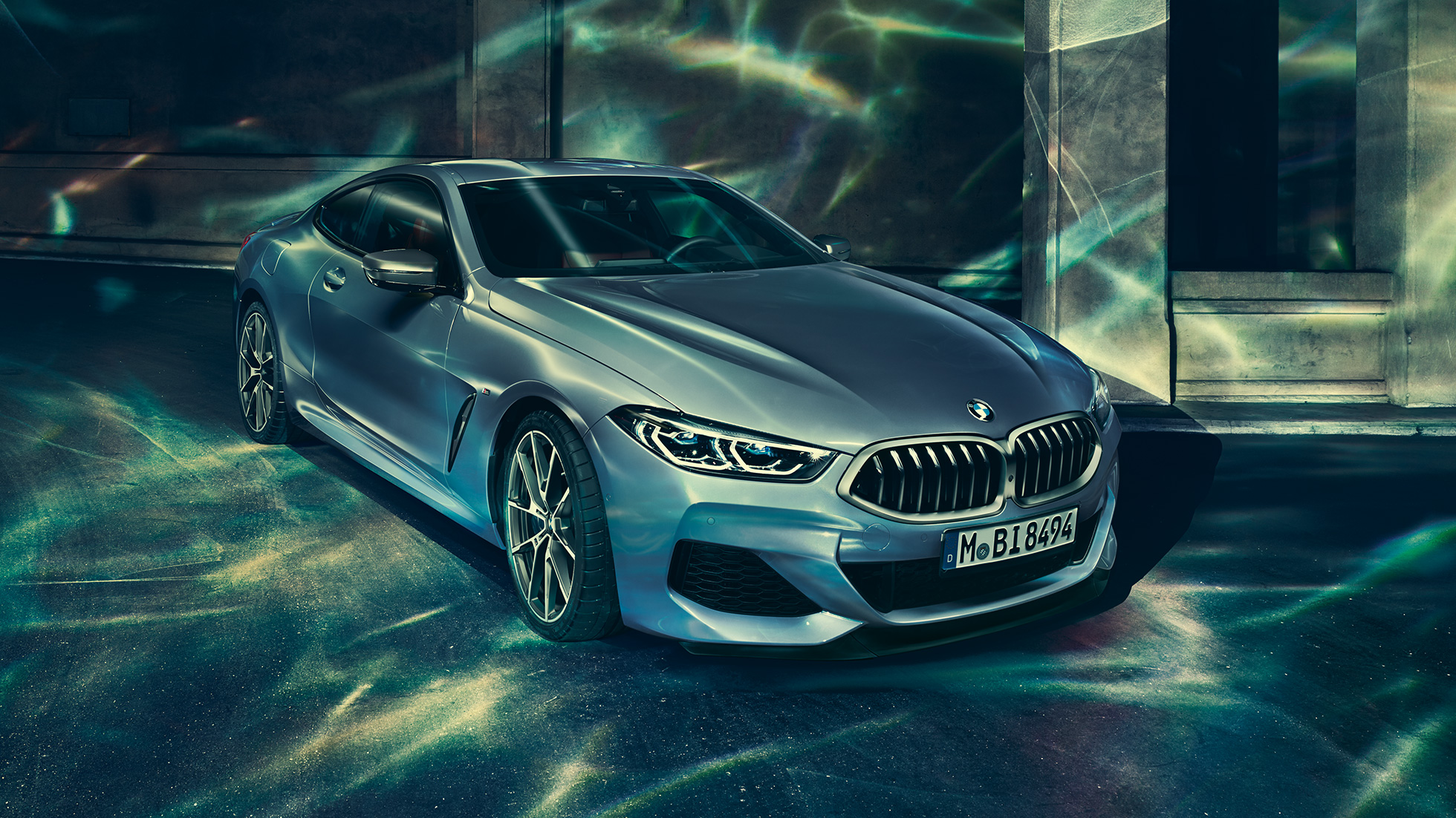 BMW M850i xDrive Coupé, v sprednjem polprofilu z leve strani. BMW M850i xDrive Coupé v kovinski barvi Barcelona Blue, v sprednjem polprofilu z leve strani, parkiran pred stavbo.