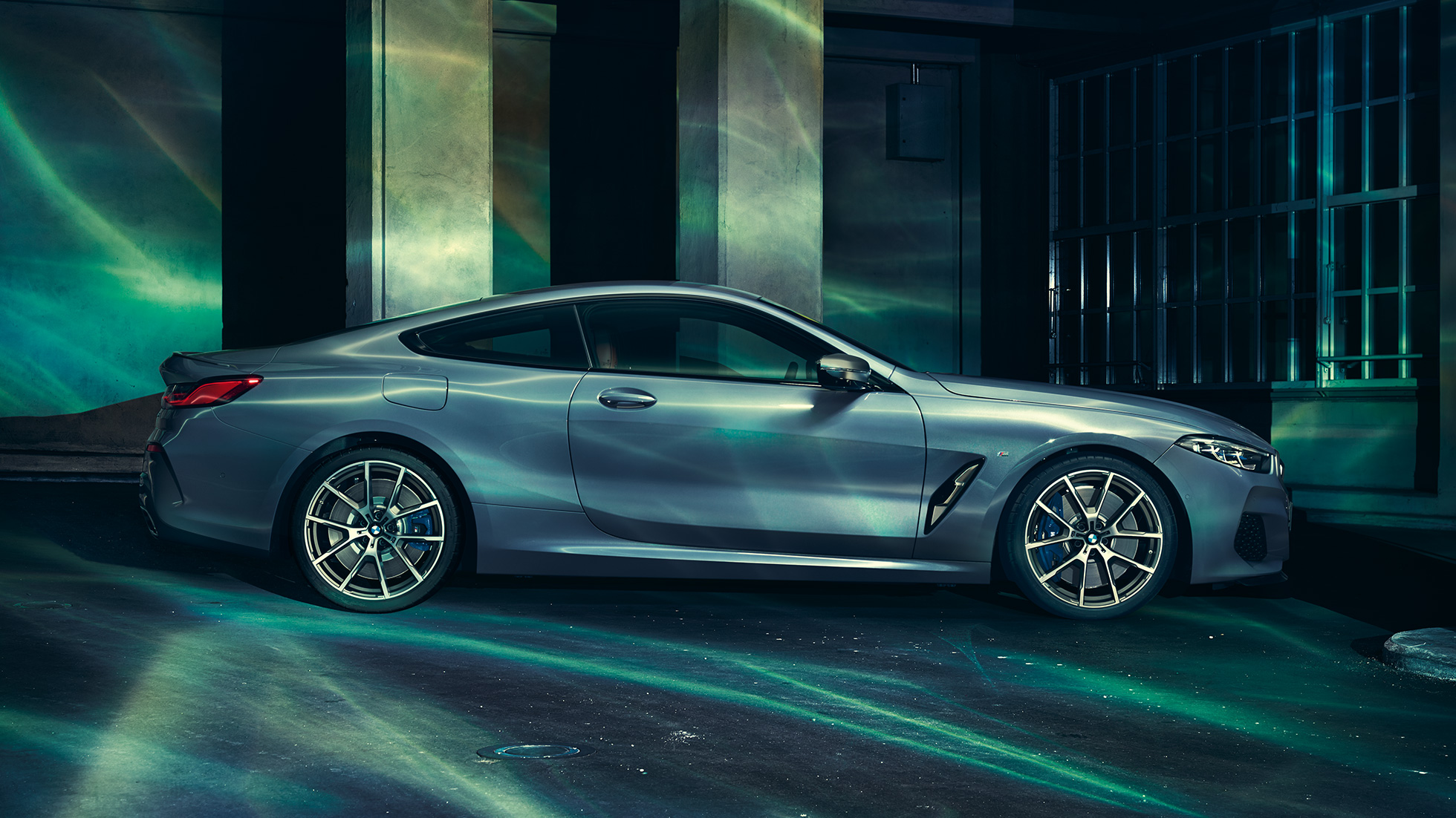 BMW M850i xDrive Coupé, v profilu. BMW M850i xDrive Coupé v kovinski barvi Barcelona Blue, v profilu, parkiran pred stavbo.