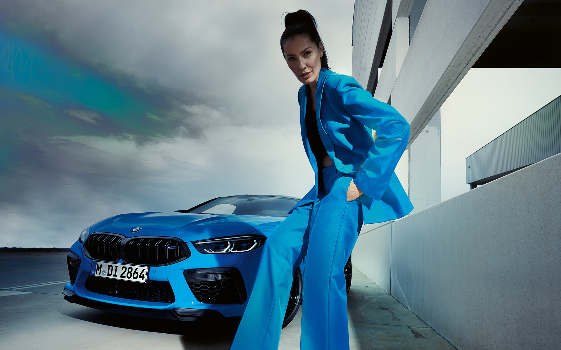 BMW M8 Competition Coupé, F92, LCI, osvežitev 2022, nekovinska barva Daytona Beach Blue, tričetrtinski pogled od spredaj z manekenko v modrem hlačnem kostimu