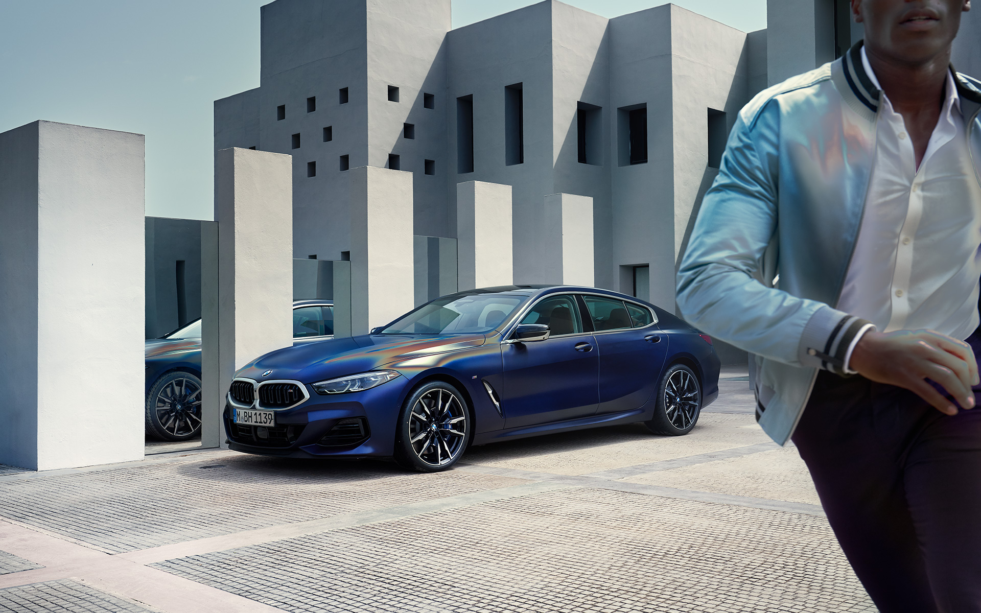Novi BMW M850i xDrive Gran Coupé, F93, LCI, osvežitev 2022, tričetrtinski pogled od spredaj Novi BMW M850i xDrive Gran Coupé, F93, LCI, osvežitev 2022, lakiranje BMW Individual v kovinski barvi Frozen Tanzanite Blue, tričetrtinski pogled od spredaj med mirovanjem z manekenom v ospredju