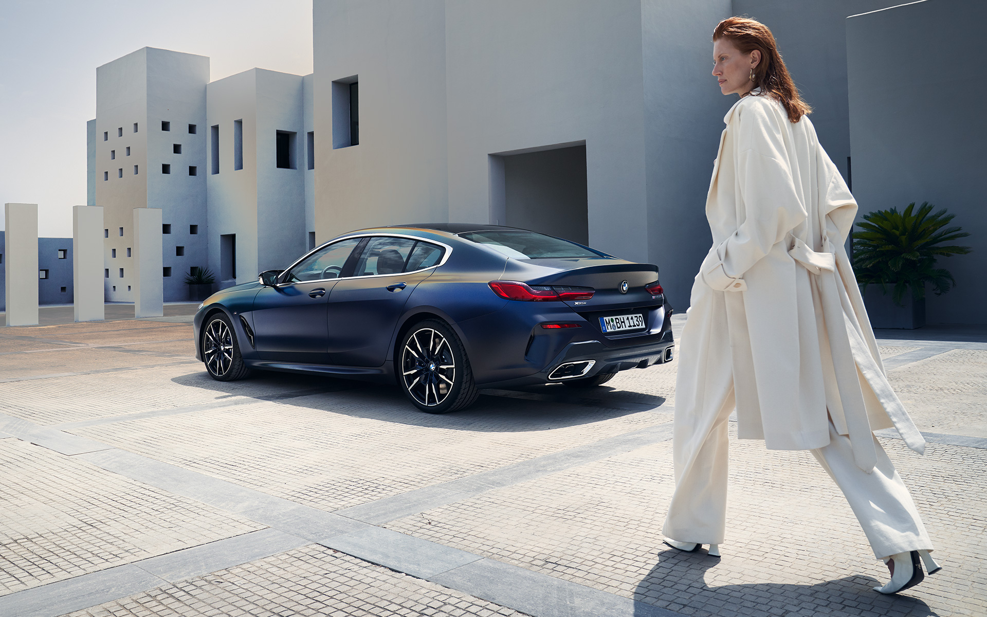 Novi BMW M850i xDrive Gran Coupé, F93, LCI, osvežitev 2022, stranski pogled z manekenko Novi BMW M850i xDrive Gran Coupé, F93, LCI, osvežitev 2022, lakiranje BMW Individual v kovinski barvi Frozen Tanzanite Blue, tričetrtinski pogled od zadaj z manekenko