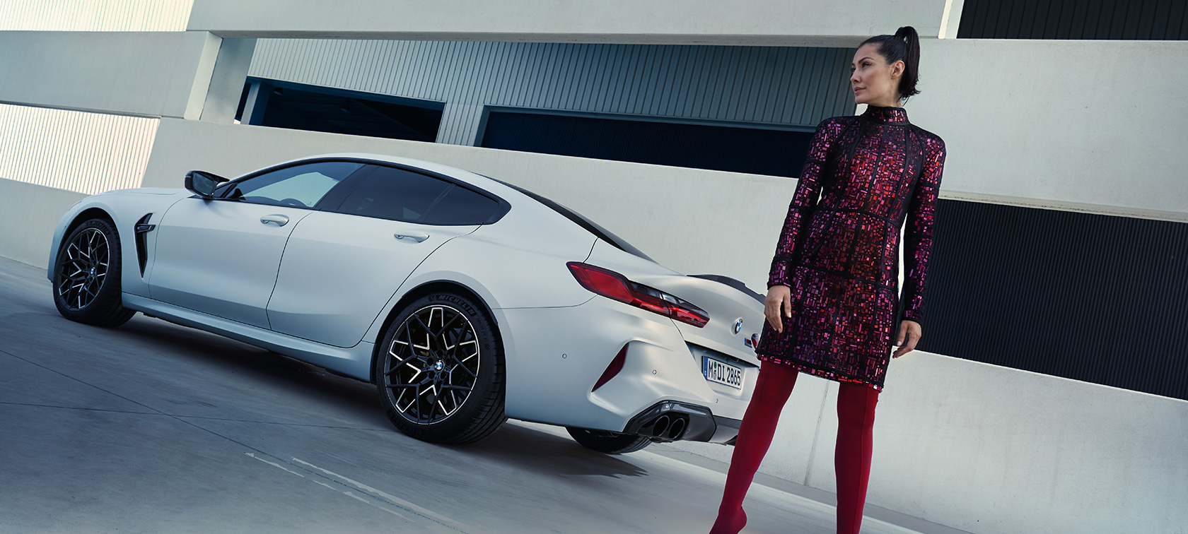 BMW M8 Competition Gran Coupé, F93, LCI, 2022, tričetrtinski pogled od zadaj BMW M8 Competition Gran Coupé, F93, LCI, osvežitev 2022, lakiranje BMW Individual v kovinski barvi Frozen Brilliant White, tričetrtinski pogled od zadaj z manekenko, ki stoji ob vozilu