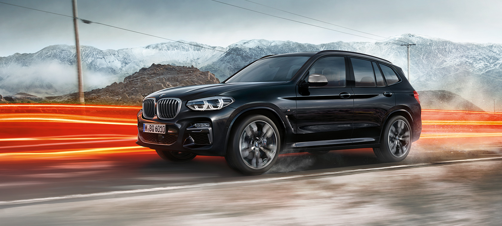 BMW X3 M40i in BMW X3 M40d, profil. BMW X3 M40i in BMW X3 M40d v kovinski barvi Black Sapphire, med vožnjo, zunanjost, pogled z zadnje strani pred gorami v ozadju s svetlobnimi črtami.
