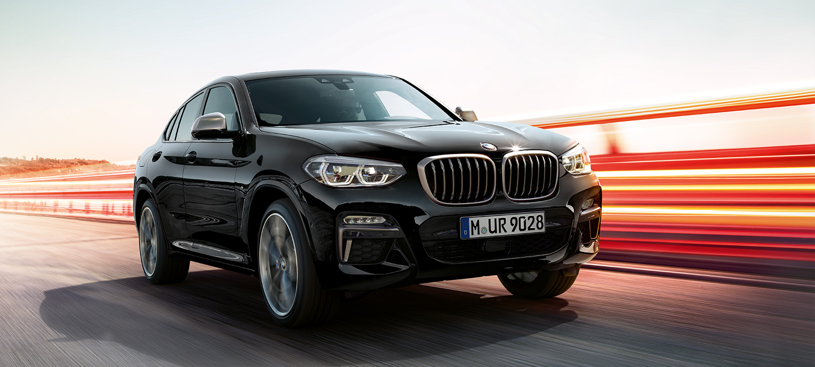 BMW X4 M40i in BMW X4 M40d, v polprofilu s sprednje leve strani. BMW X4 M40i in BMW X4 M40d v kovinski barvi Black Sapphire, zunanjost, v polprofilu s sprednje strani, leva stran, svetlobne sledi.