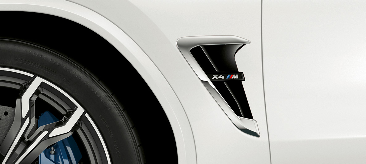 BMW X4 M, bočna maska M. BMW X4 M v barvi Alpine White, zunanjost, bočna maska M s kromiranimi poudarki in oznako modela.