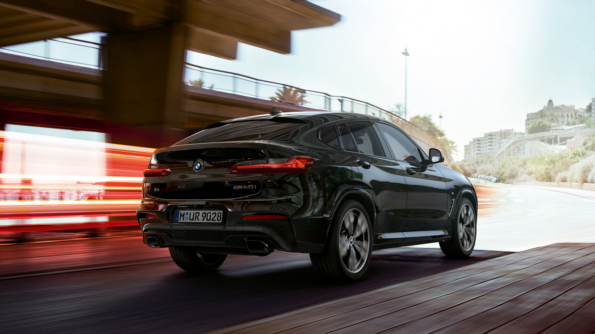 BMW X4 M40i, v polprofilu s sprednje strani. BMW X4 M40i v kovinski barvi Black Sapphire, med vožnjo, zunanjost, v polprofilu od spredaj s svetlobnimi črtami.