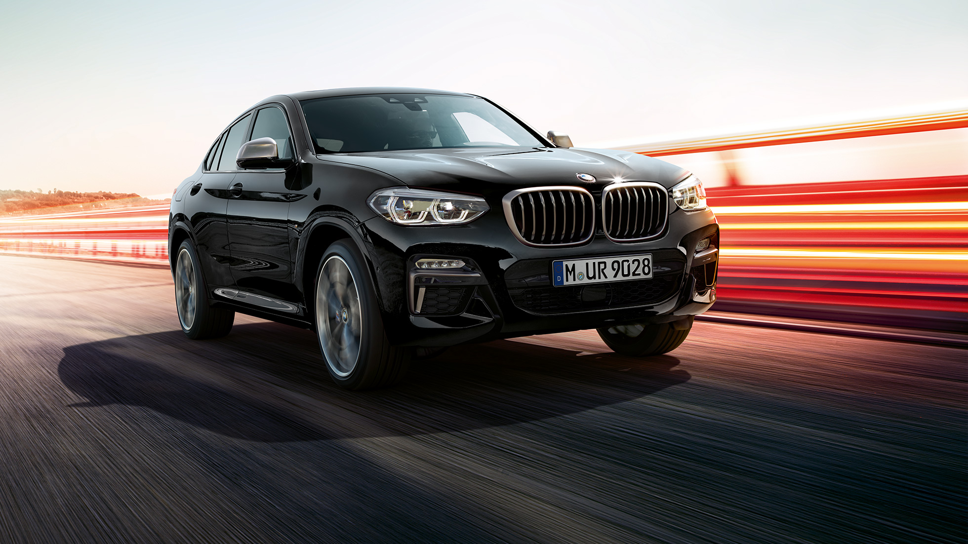 BMW X4 M40i in BMW X4 M40d, v polprofilu s sprednje strani. BMW X4 M40i in BMW X4 M40d v kovinski barvi Black Sapphire, zunanjost, v polprofilu s sprednje strani, leva stran s svetlobnimi sledmi.