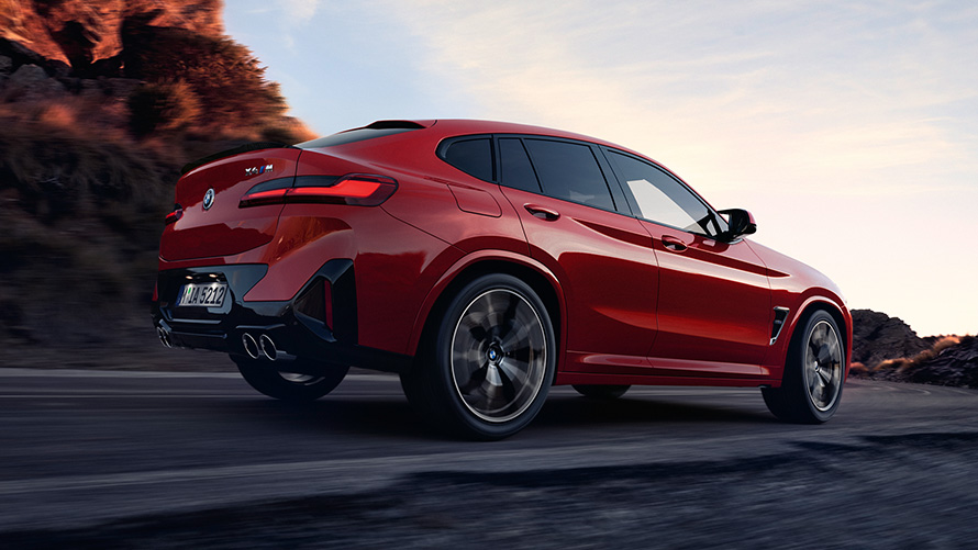 BMW X4 M, F98, LCI, osvežitev 2021, kovinska barva Toronto Red, tričetrtinski pogled od zadaj med vožnjo po cesti