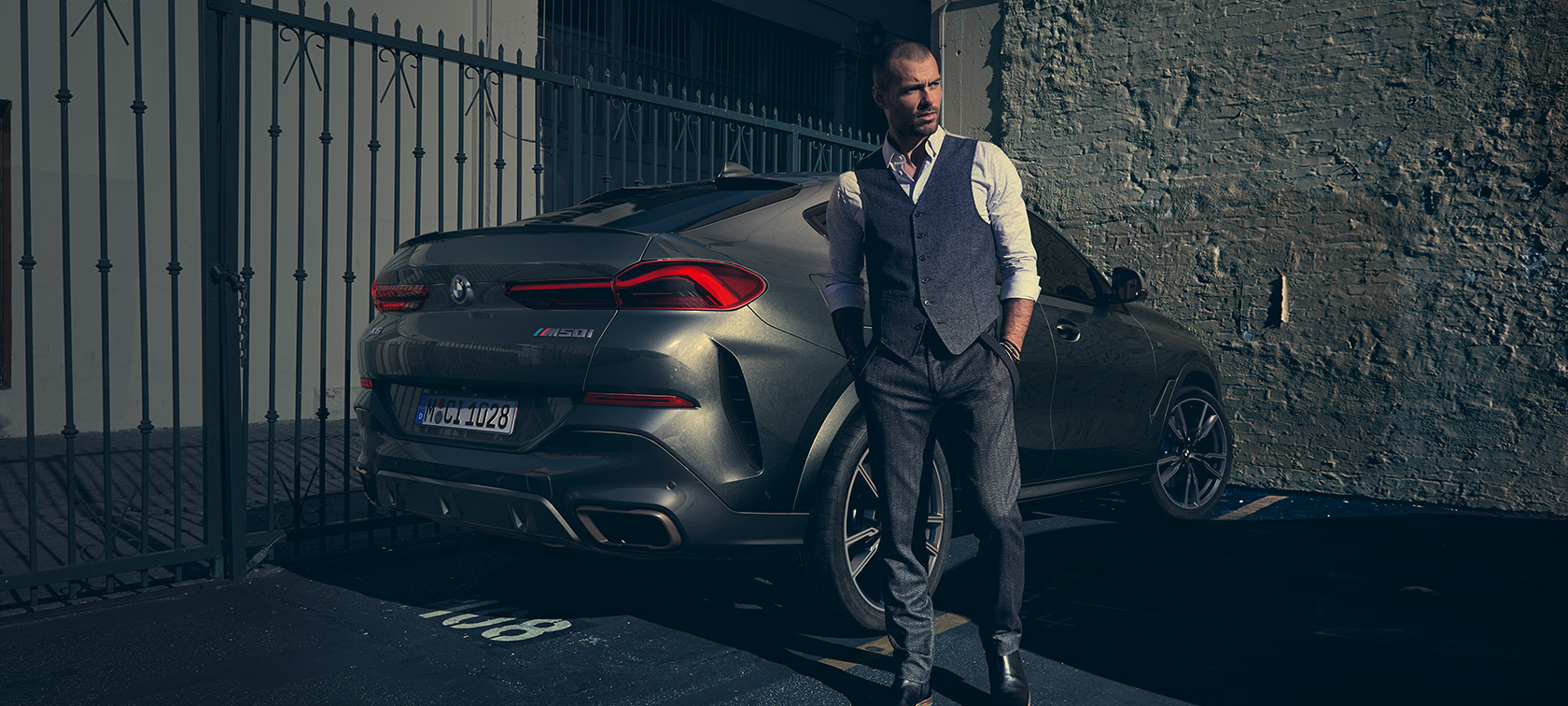 BMW X6 M50i, tričetrtinski pogled od zadaj Moški stoji ob BMW X6 M50i, SUV, tričetrtinski pogled od zadaj