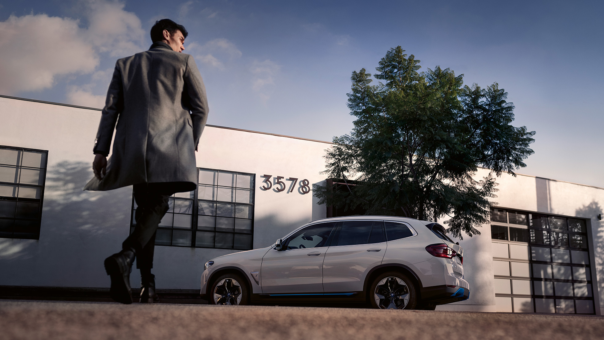 BMW iX3, G08, stranski pogled pred stavbo z moškim BMW iX3, G08, 2020, kovinska barva Mineral White, stranski pogled pred stavbo z moškim