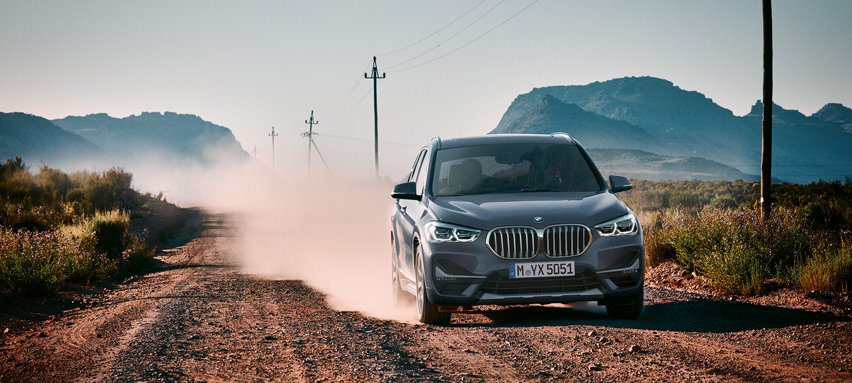 BMW X1, tričetrtinski pogled od zadaj. BMW X1, tričetrtinski pogled od zadaj med vožnjo pred gorsko pokrajino.